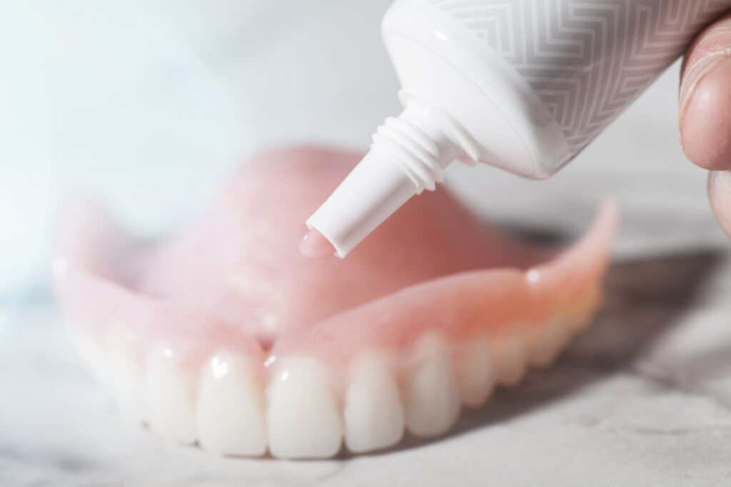Pink denture adhesive being applied to a set of dentures sitting on a white and grey marble counter.