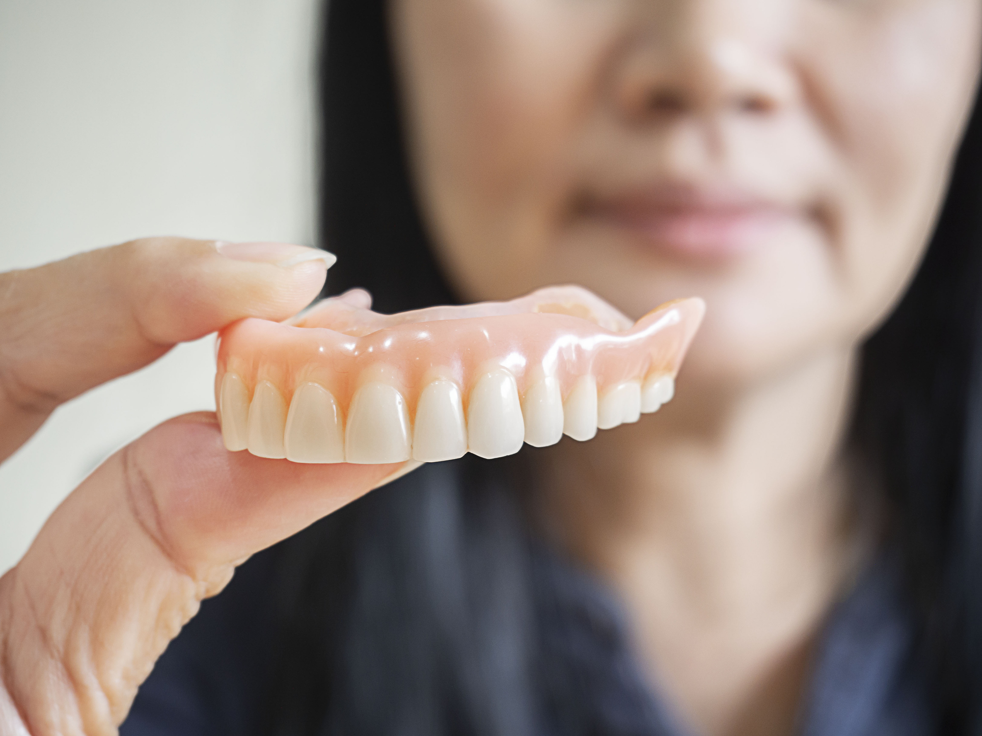 A woman holding up her dentures after getting them relined and rebased for a comfortable fit.