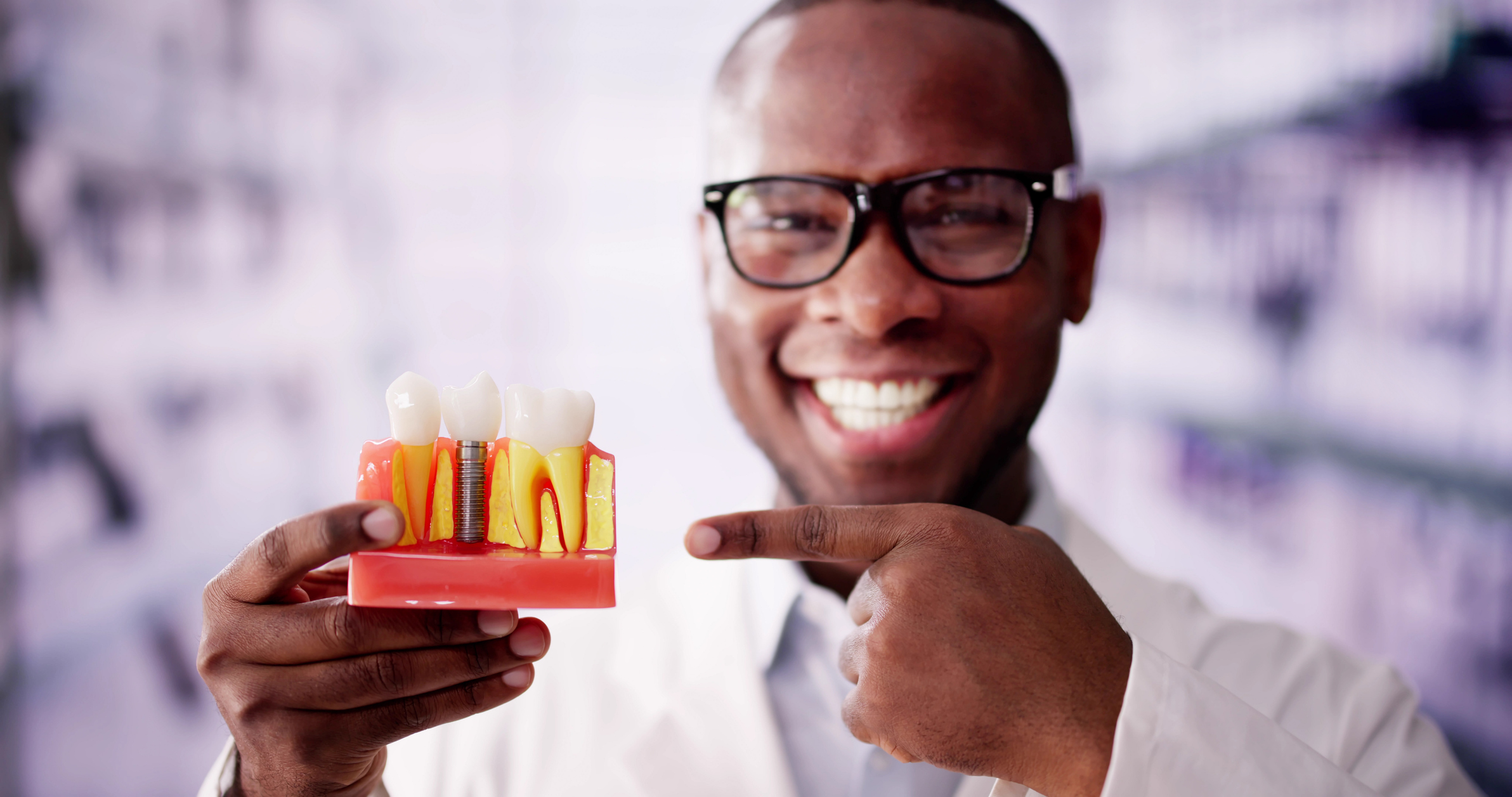 A dentist holds up a model of implant-supported restorations with a bright smile.